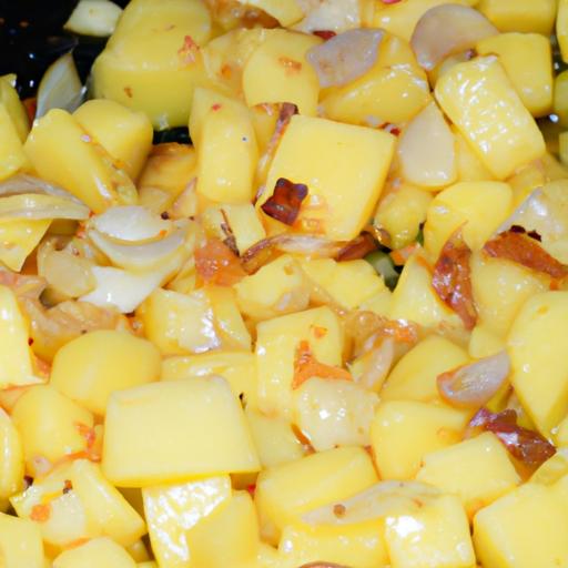 Một tấm hình chụp cận cảnh của một chiếc chảo đang xào khoai tây đã được thái thành từng miếng nhỏ, kèm với tỏi và hành thơm phức.